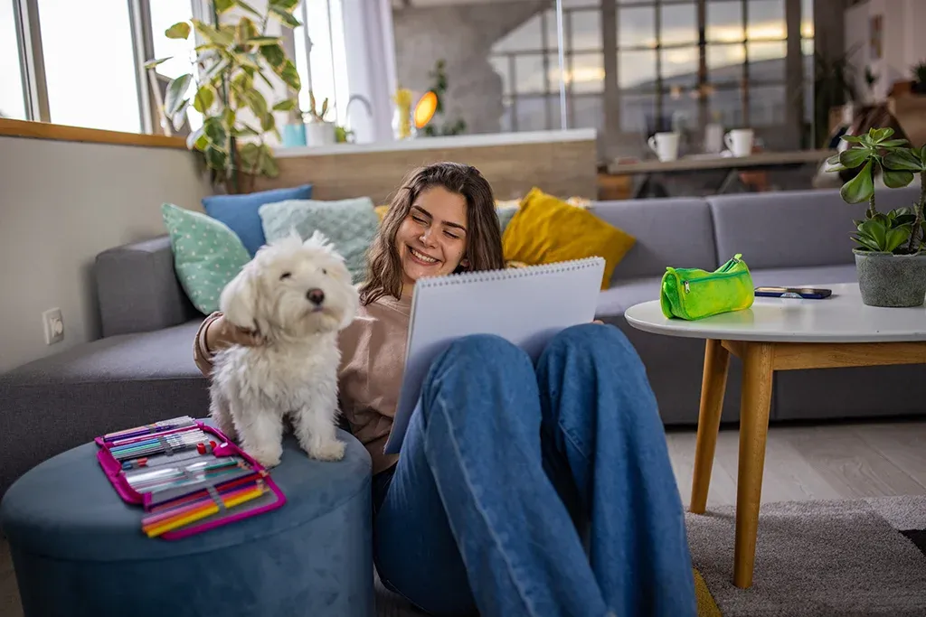 A woman sitting on a couch with a white dog and a laptop.