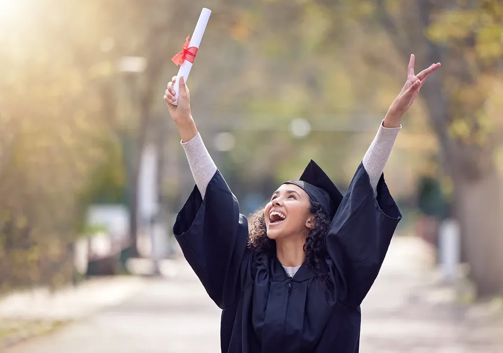A woman celebrating her graduation with her arms up.