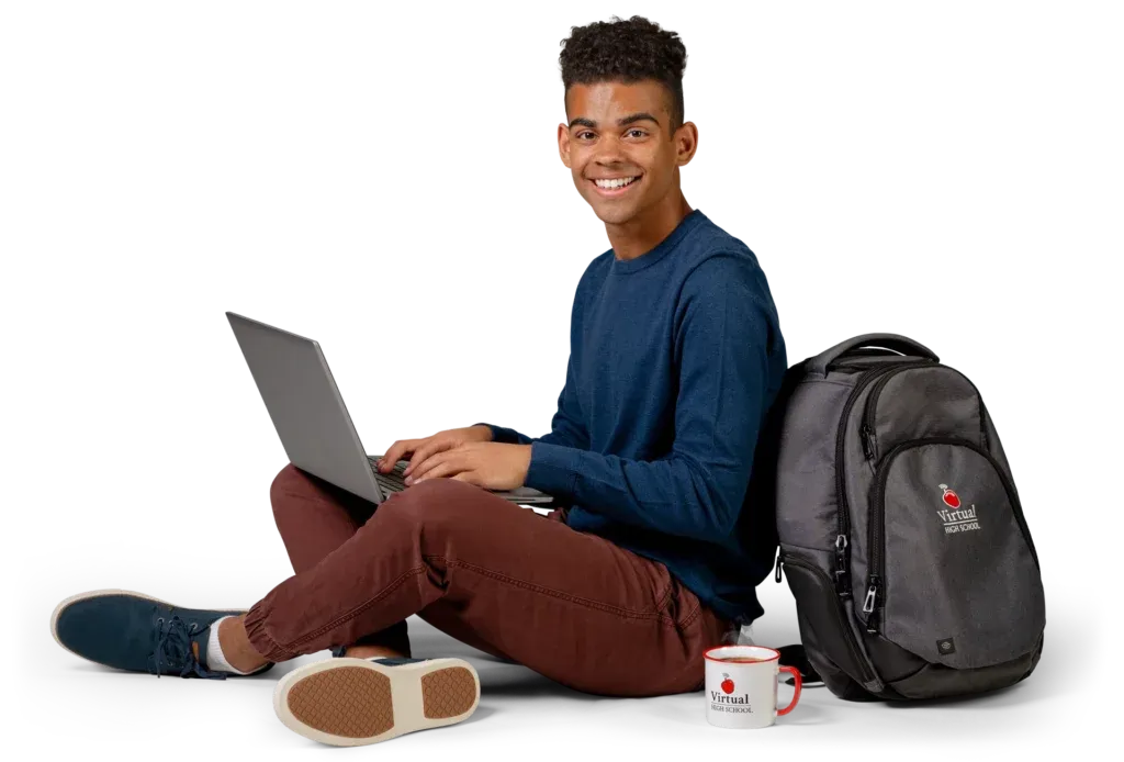 A young man sitting on the floor with a laptop, backpack, and a mug.