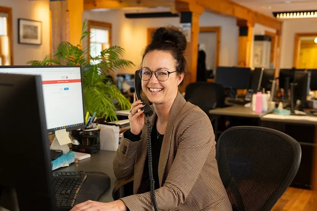 A woman smiling while talking on the phone in an office.