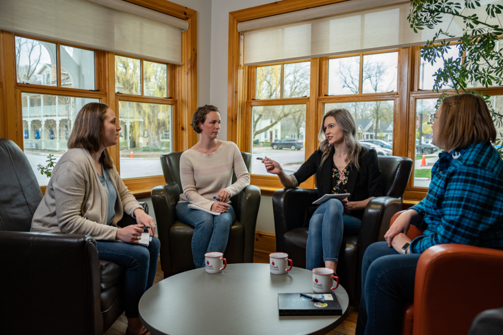 Four women sit around a coffee table discussing policies.