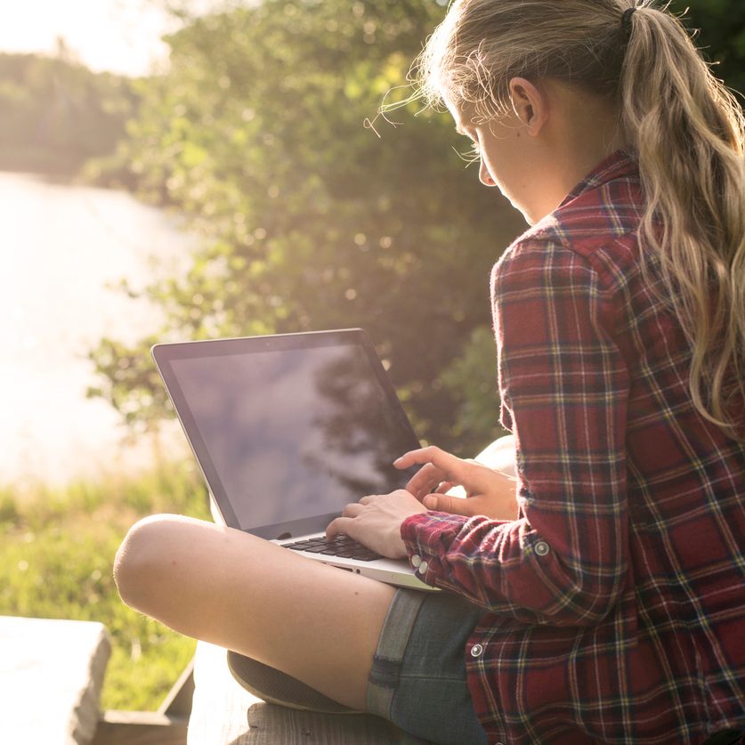Student using their laptop outside in the sun, near a lake